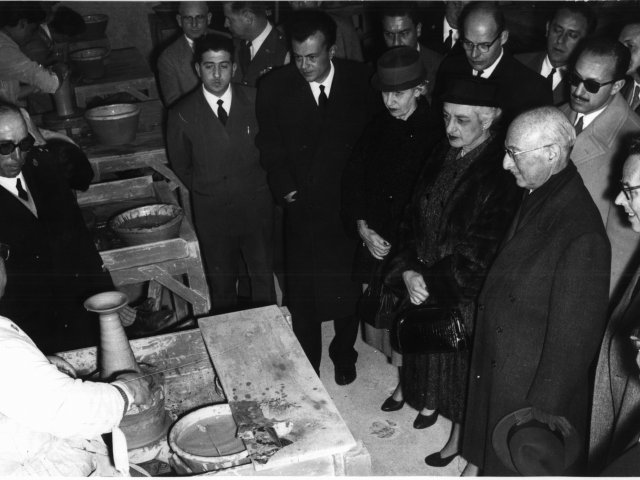 Visita Ambasciatore Zellerbach - L’Ambasciatore Zellerbach, la sua consorte ed altri membri dell’Ambasciata, nell’aula di foggiatura. Al tornio il prof. Vincenzo Spagnulo; da destra, in primissimo piano l’On. Gaspare Pignatelli; in prima fila, l’Ambasciatore, la consorte, due rappresentaScarica il file