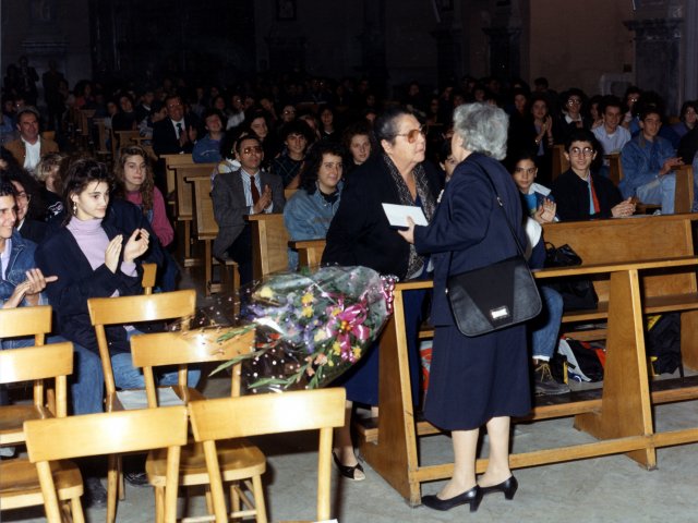 Cerimonia di inaugurazione as 1988/89 - Nella chiesa Madre si tiene la cerimonia religiosa per l’inaugurazione dell’anno scolastico 1988/89. La collaboratrice Dorotea Quaranta riceve dalla sua collega Grazia Occhibianco un mazzo di fiori (forse in occasione della sua collocazione a riposo).Scarica il file