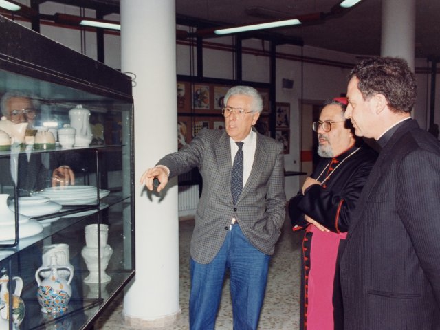 Visita e benedizione della scuola da parte di SE Mons Benigno Papa - Il Preside Vincenzo De Filippis, porta in visita gli ospiti nella varie aule speciali della scuola. In questa foto sono davanti ad una vetrina con oggetti della sezione Ceramica. In particolare il Preside, sicuramente, mette in evidenza i centrotavola preScarica il file